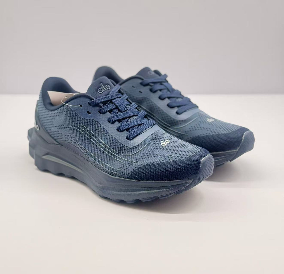 Three-quarter front view of a pair of dark blue Alo sneakers with visible branding on the tongues and toes.