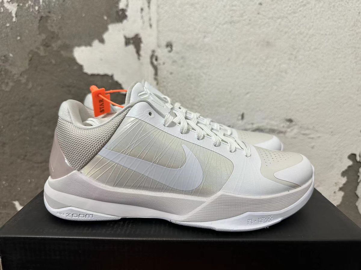 Side view of a silver and white Nike Kobe basketball shoe with a low-cut profile and Zoom-marked midsole.