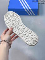 Underside of the sneaker showing a white textured outsole with circular and trefoil-shaped tread details.