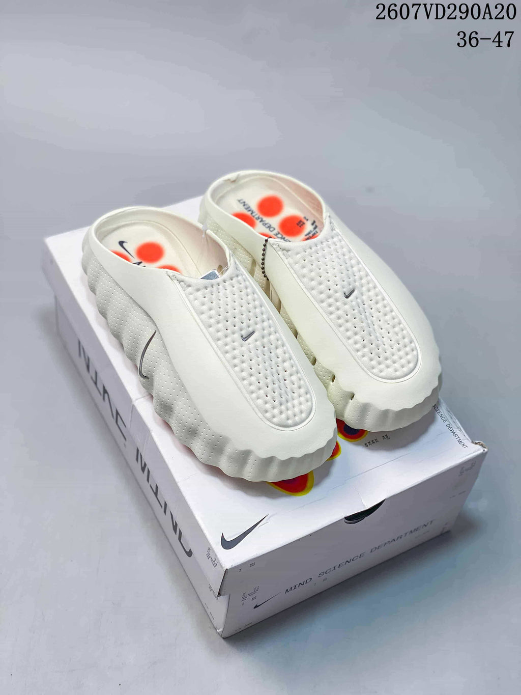 Pair of white Nike Mind 001 covered-toe slides displayed on a box, showing perforated uppers and textured soles.