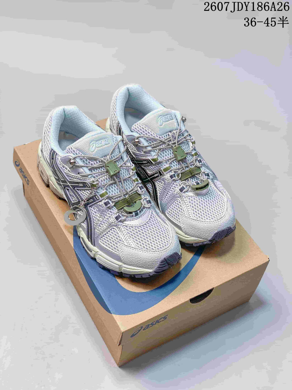 Front three-quarter view of gray and white ASICS Gel-Kahana 8 FL sneakers with contrasting green lace details and decorative hardware.