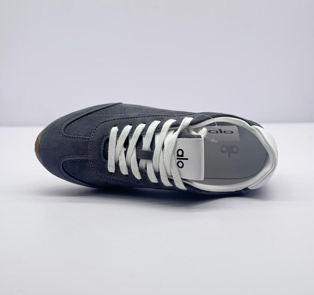 Top view of one carbon gray sneaker showing the lace arrangement, tongue branding, and white lining.