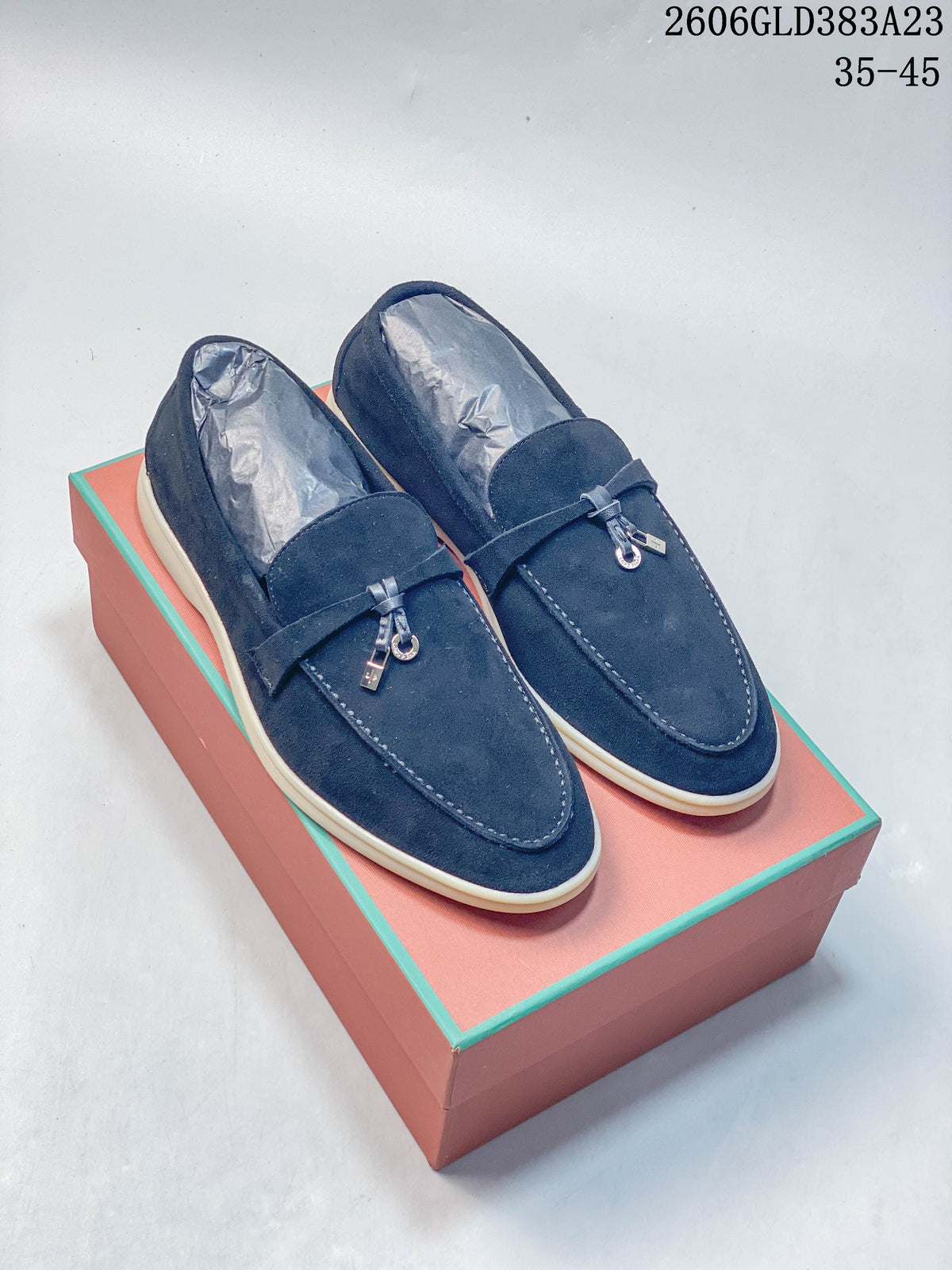 Pair of navy loafers with metal vamp details and light-colored soles on a box
