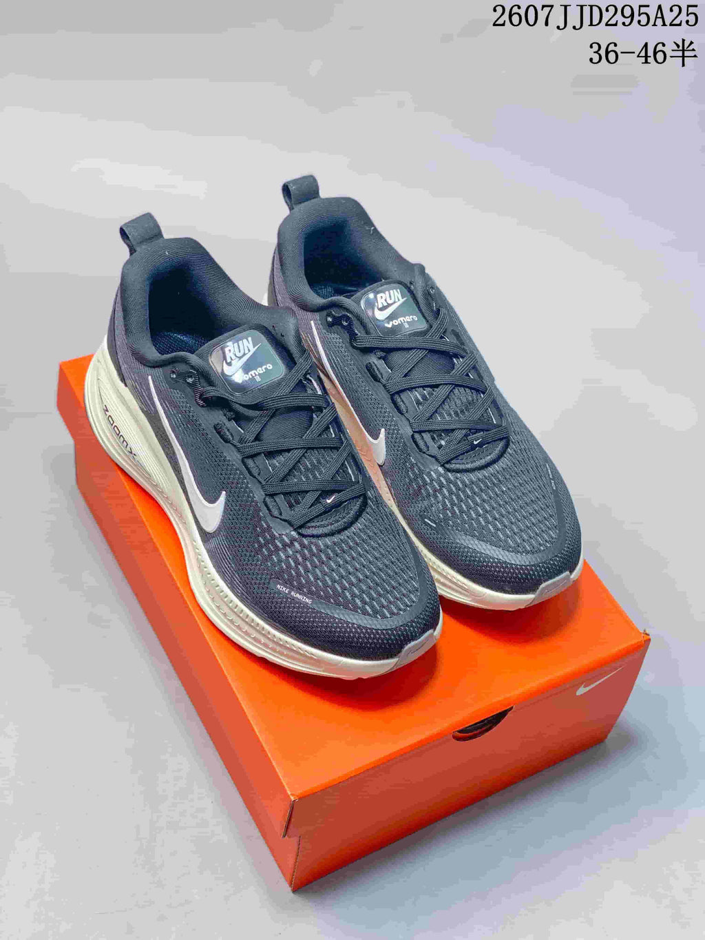 Nike Vomero 18 sneakers shown from the front on an orange shoebox, with dark uppers, white Swoosh logos, and a light-colored midsole; image text shows TD295A25 and size range 36–46.5.