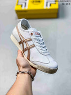 White Onitsuka Tiger sneaker held in hand, showing metallic brown contrast stripes and a light-colored outsole.