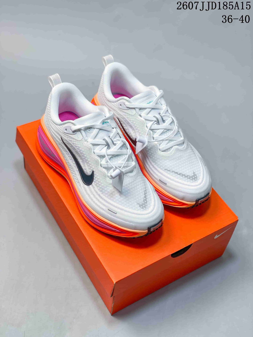 Pair of white Nike Vomero Plus running shoes with orange and pink midsoles displayed on an orange shoebox.