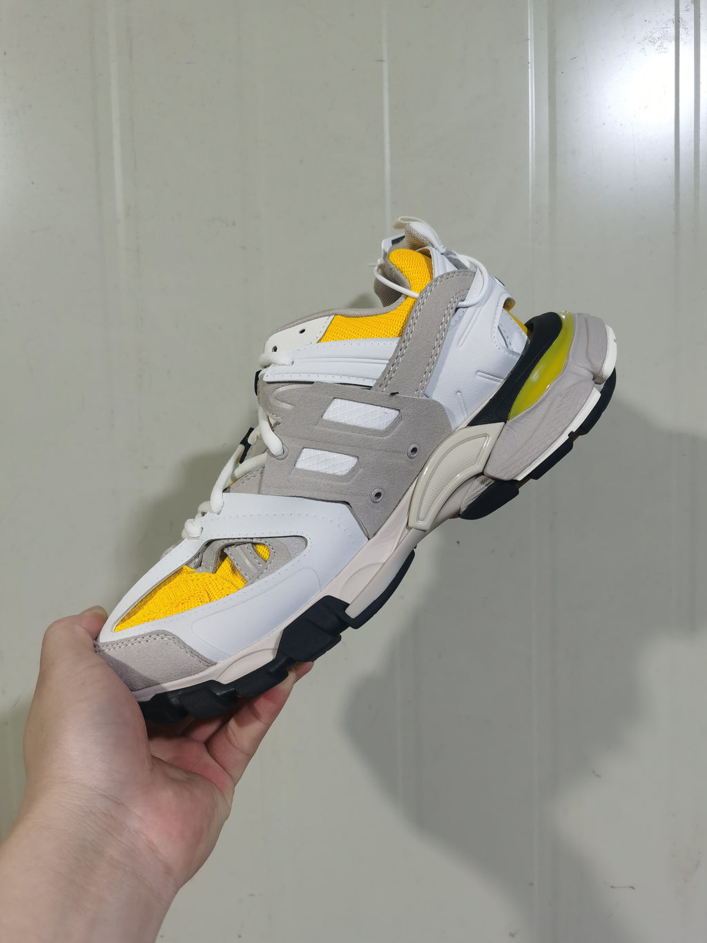 Side and outsole view of the yellow, white and grey Balenciaga Track sneaker, showing layered panels, mesh sections and a chunky black-and-white sole.