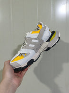 Side and outsole view of the yellow, white and grey Balenciaga Track sneaker, showing layered panels, mesh sections and a chunky black-and-white sole.