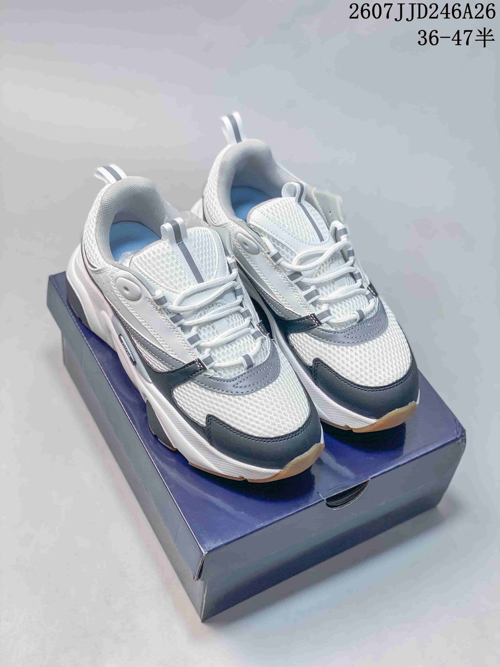 Pair of white Dior low-top sneakers with black and gray details displayed on a box.