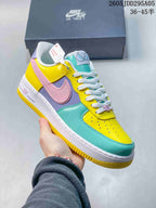 Angled side view of the multicolor Nike Air Force 1 sneaker showing the pink Swoosh, turquoise forefoot, yellow heel panel and white midsole.