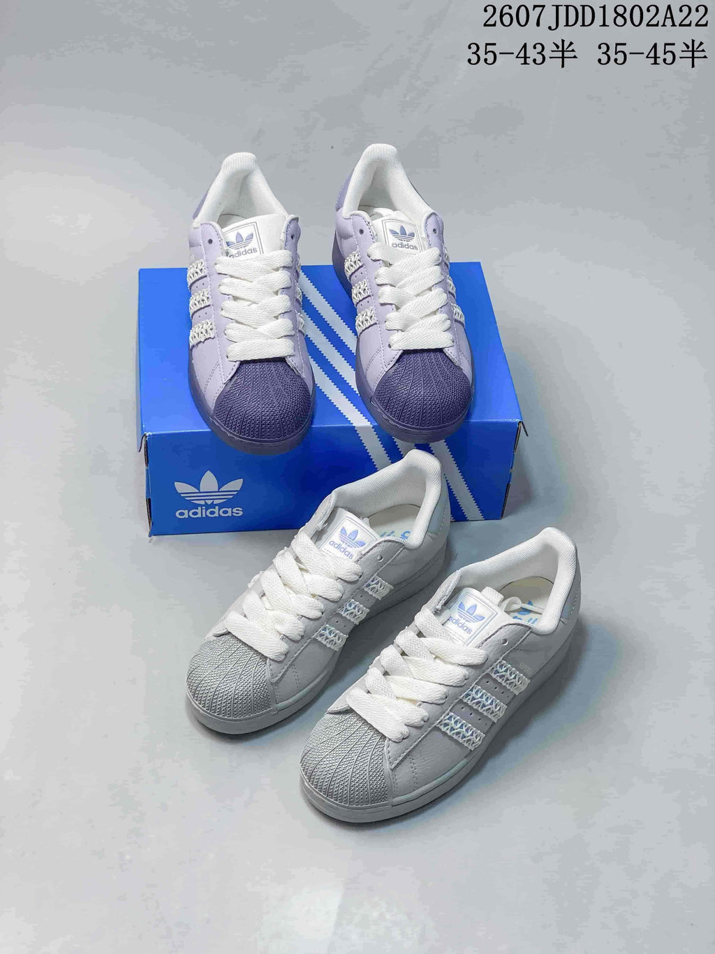 Multiple views of light-colored Adidas Superstar sneakers arranged around a blue Adidas shoe box.