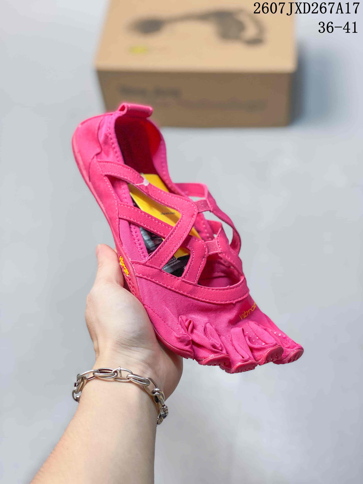 Close view of a pink Vibram five-toe shoe held in hand, showing the open strap sections and low-top profile.