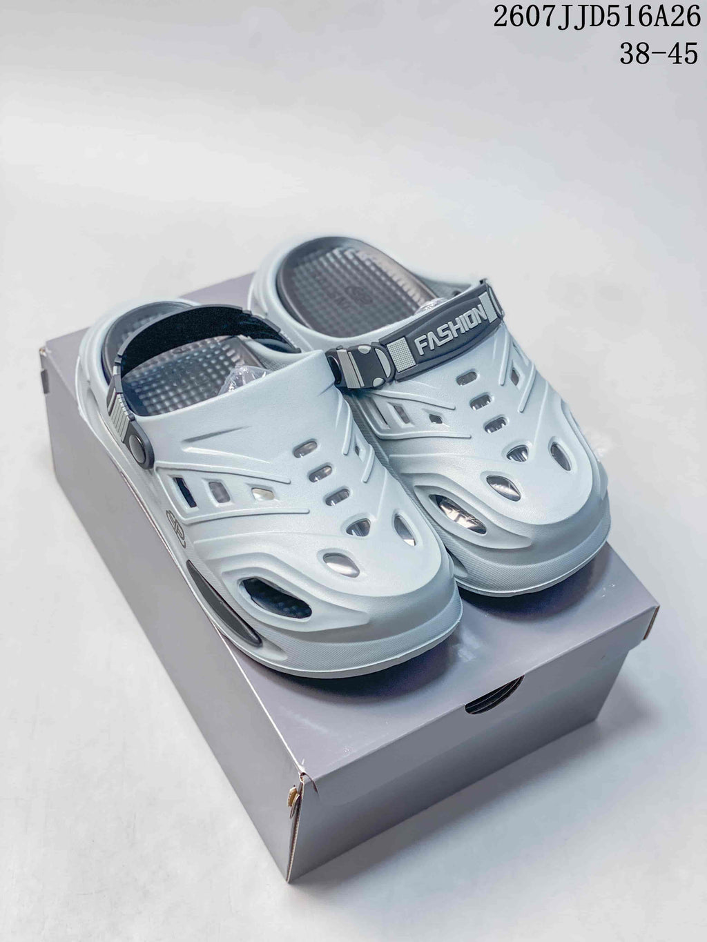 Light gray platform clog sandals shown from the front on a shoe box, with ventilation cutouts and an adjustable heel strap.