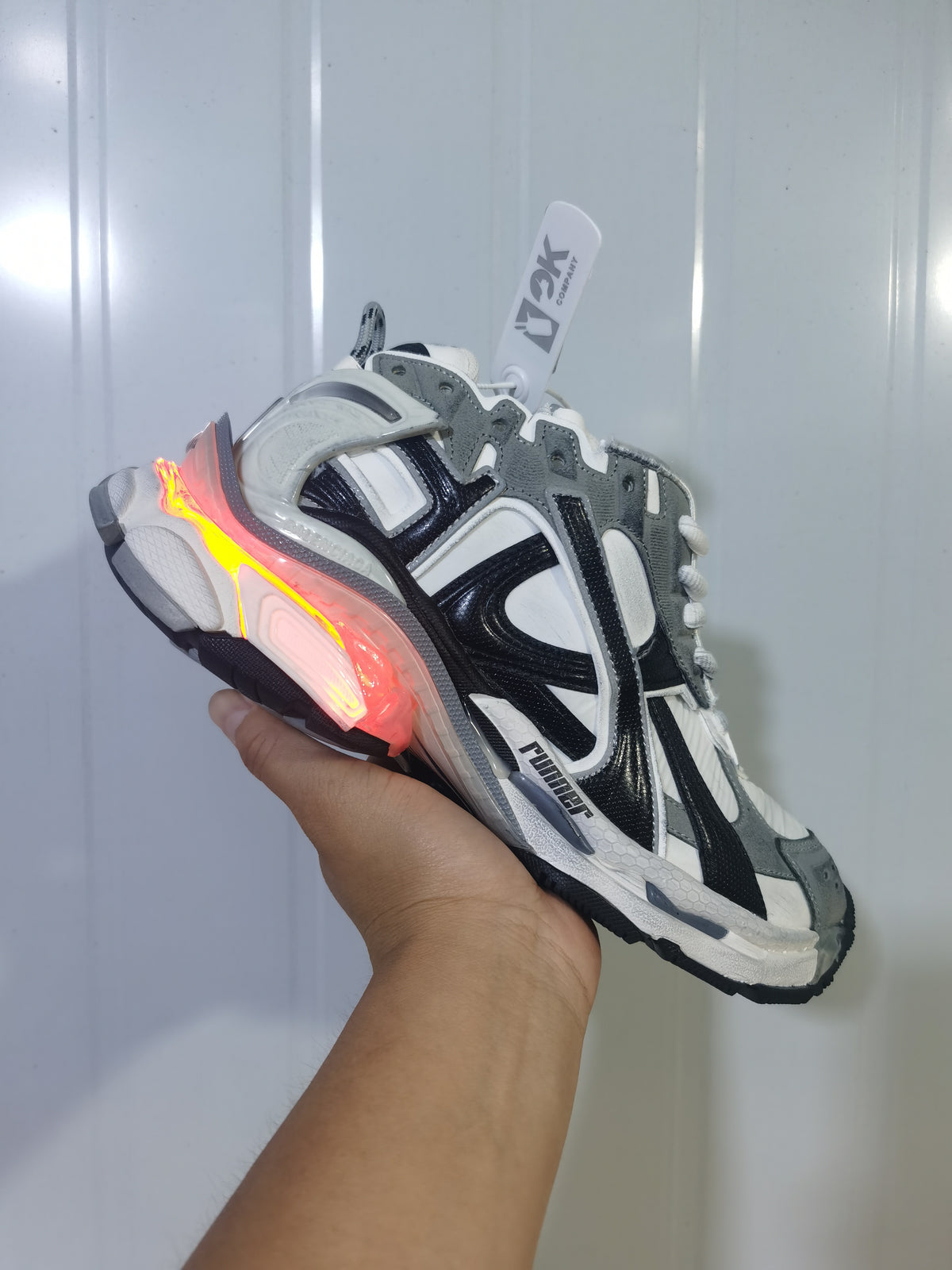 Angled view of the Puma 9012 sneaker showing layered panels, black branding details, and a red-orange illuminated heel accent.