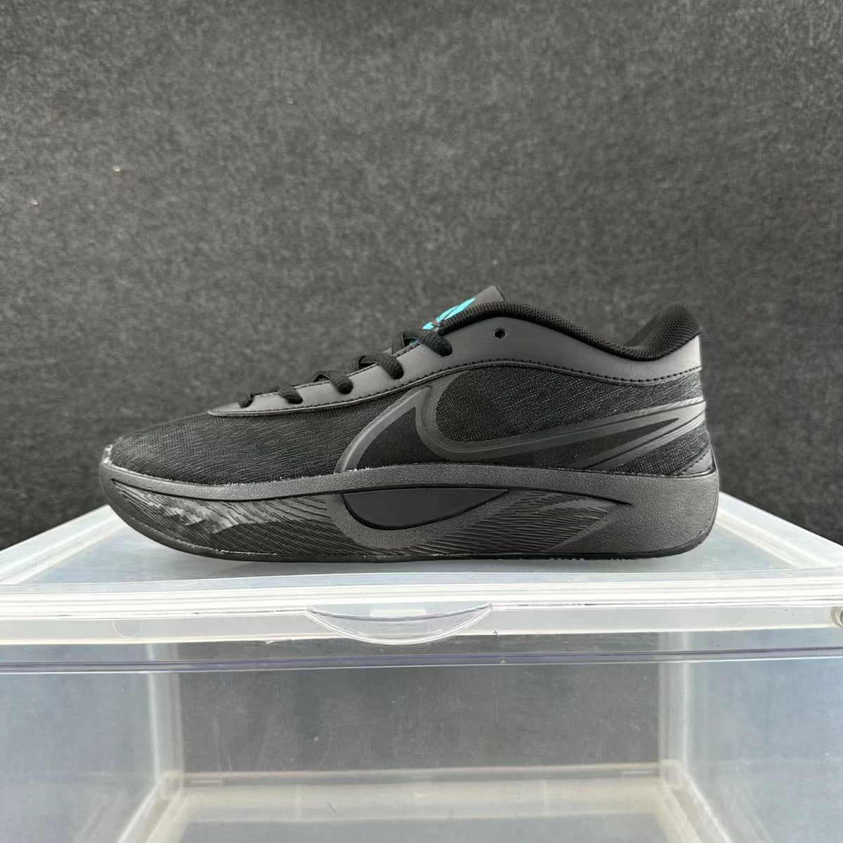 Side view of an all-black Nike lace-up sneaker with a sculpted sole and a small turquoise accent near the tongue.
