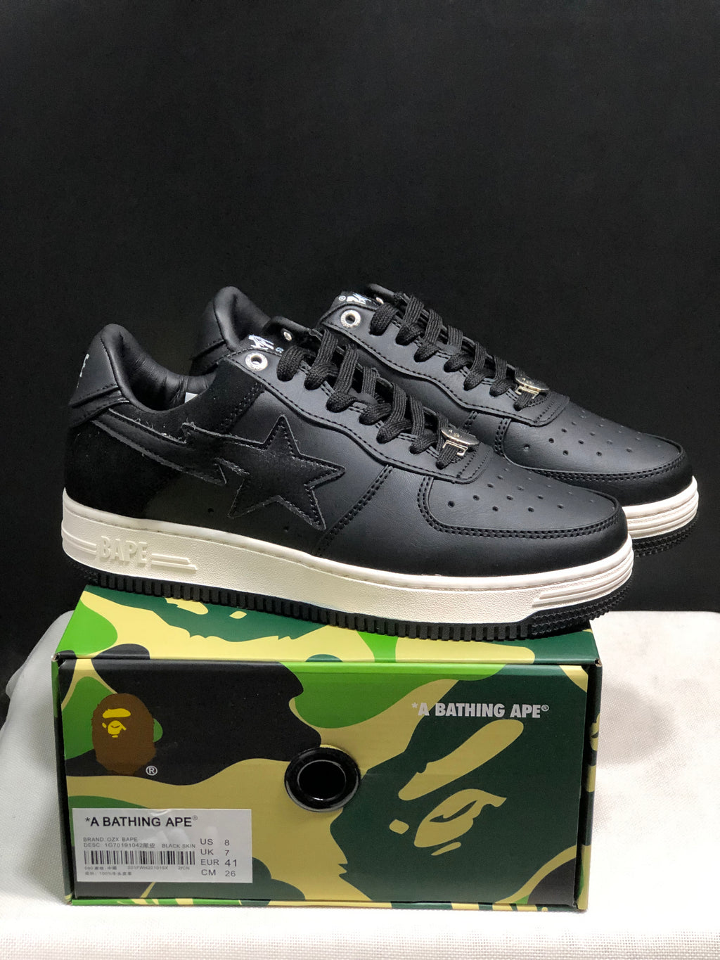 Black and white Bape Sta sneakers displayed on a branded camouflage shoe box.