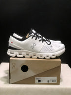 Side view of an Ivory and Black On Cloud X4 sneaker with the shoe box label visible.