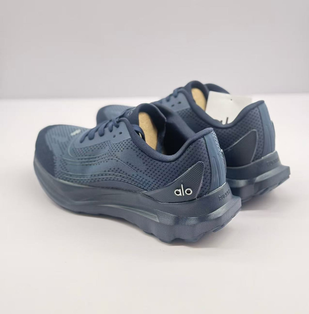 Rear view of the dark blue Alo sneaker pair with visible heel details and textured upper panels.