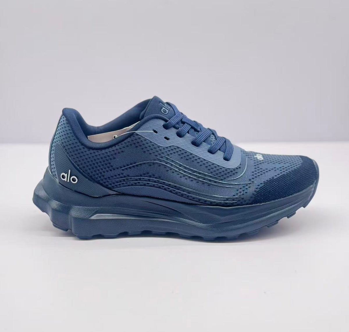 Side view of a dark blue Alo lace-up sneaker showing the patterned upper, layered side detailing, and raised sole.