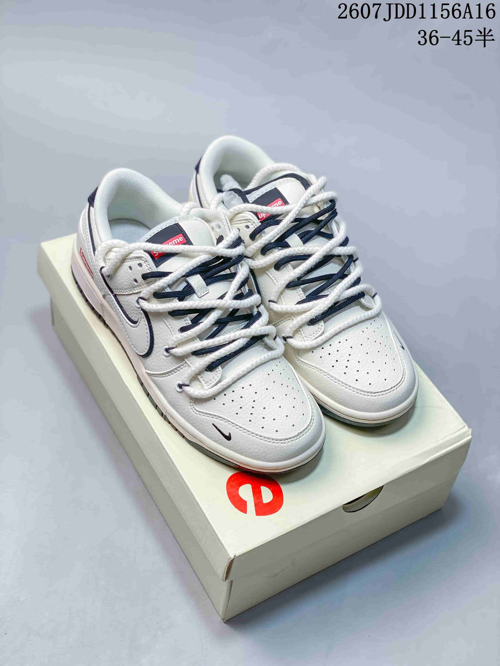 Pair of off-white Nike SB Dunk Low sneakers with dark blue detailing displayed on a branded shoe box.