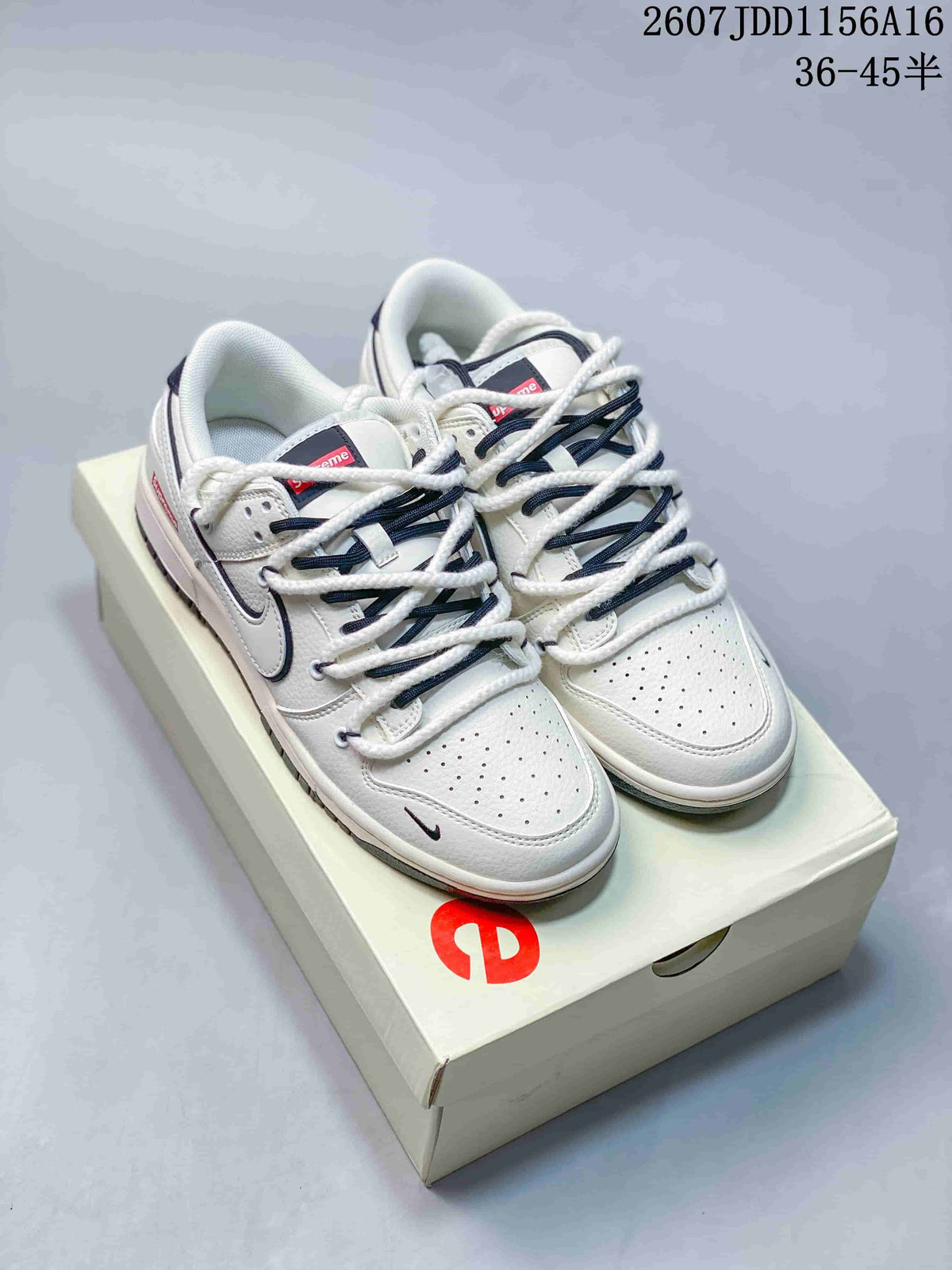 Pair of off-white Nike SB Dunk Low sneakers with dark blue detailing displayed on a branded shoe box.
