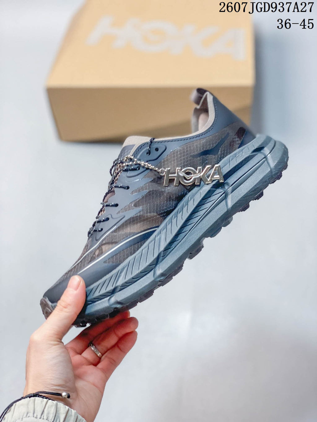 Side view showing the layered mesh-style upper, lace area, gray midsole, and visible HOKA branding.