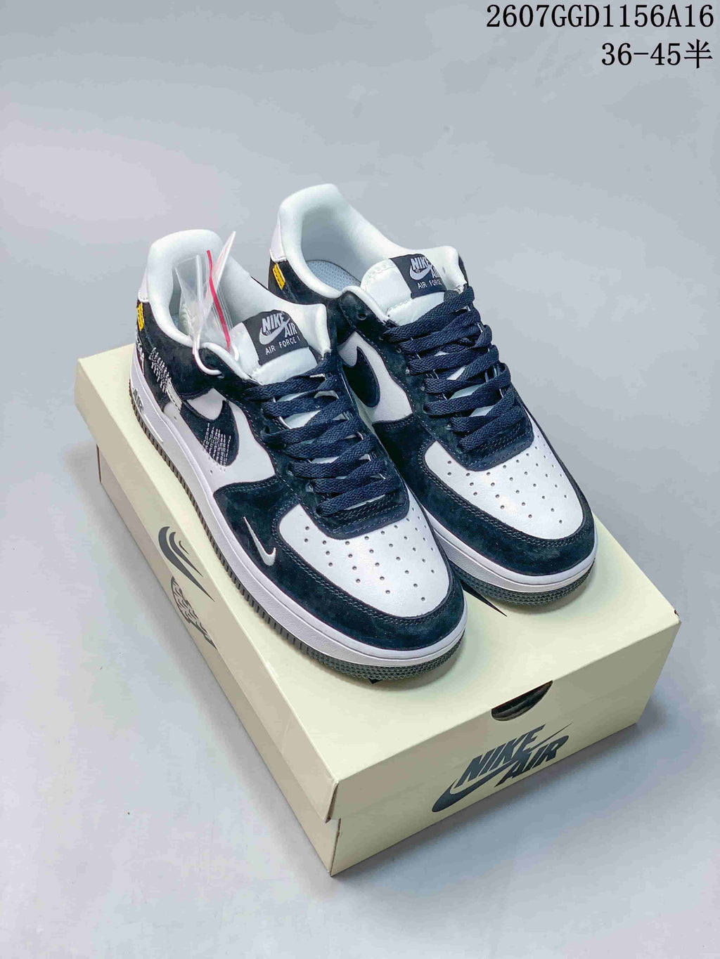 Pair of black and white Nike Air Force 1 sneakers displayed on a shoebox, showing contrasting overlays, dark laces, and white perforated toe boxes.