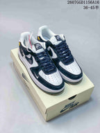 Pair of black and white Nike Air Force 1 sneakers displayed on a shoebox, showing contrasting overlays, dark laces, and white perforated toe boxes.