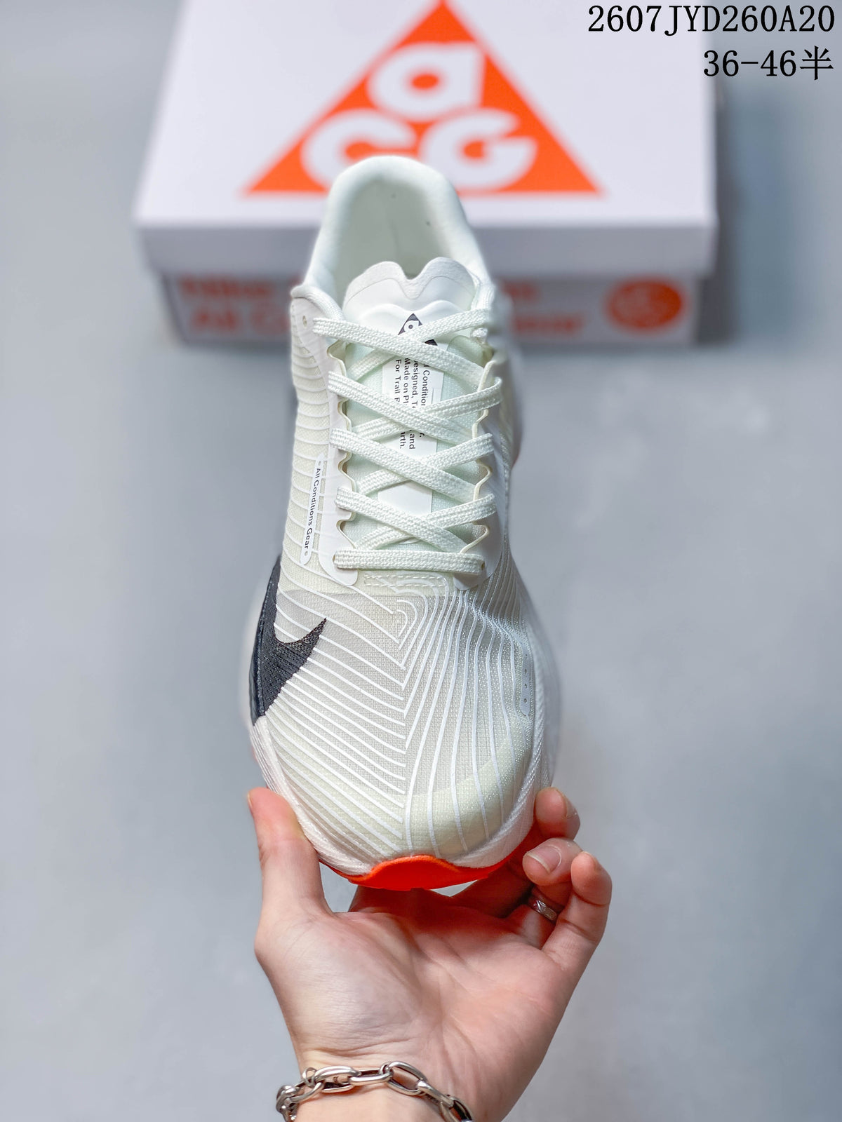 Front view of an off-white Nike ACG Ultrafly Trail sneaker showing the laces, patterned upper, and orange toe outsole.