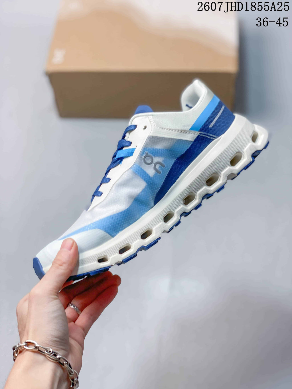 Side view of the white and blue On sneaker showing the layered upper, side logo, thick midsole, and blue outsole lugs.