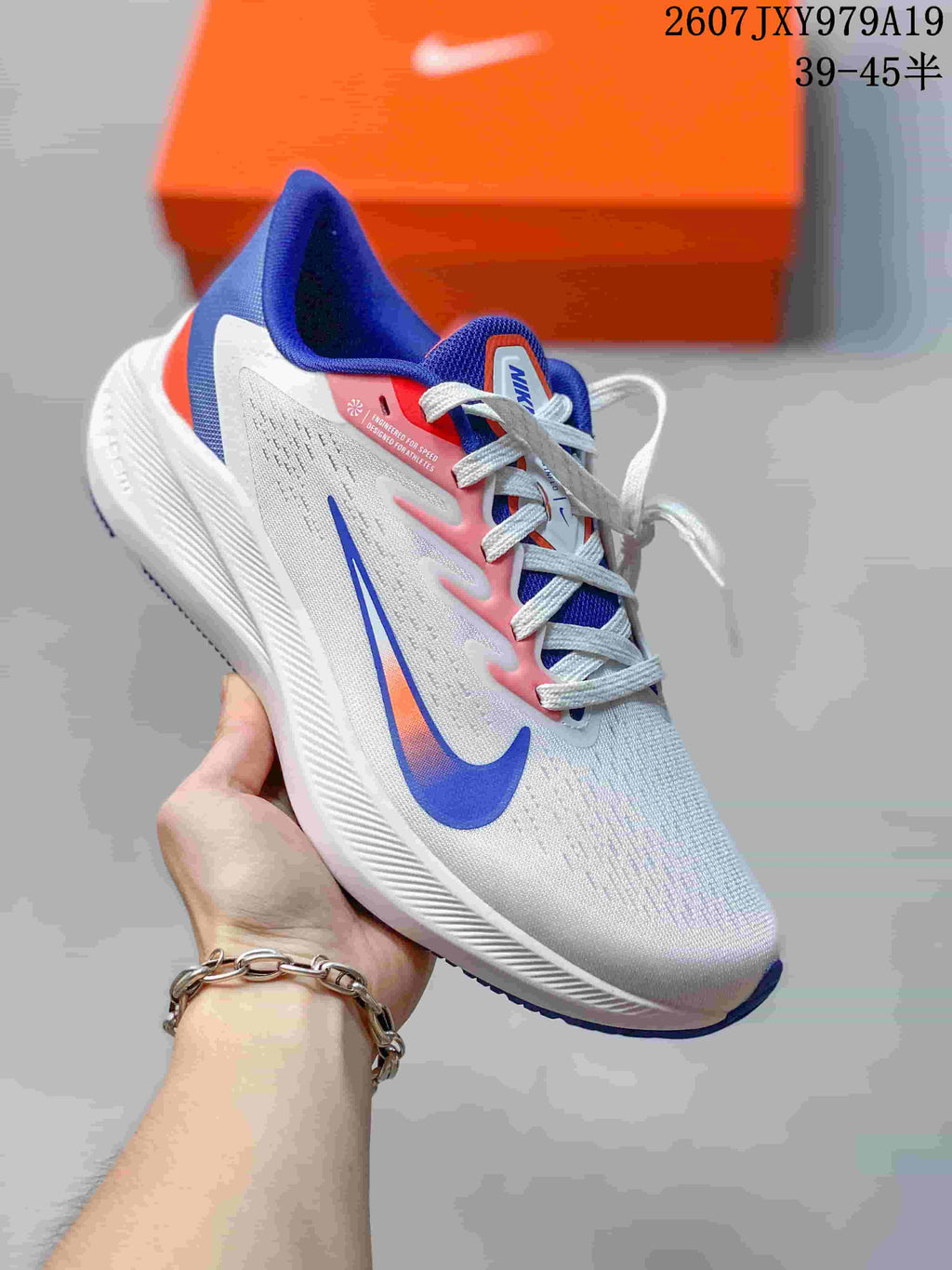 White Nike running sneaker with blue and pink accents, held in front of an orange shoe box.