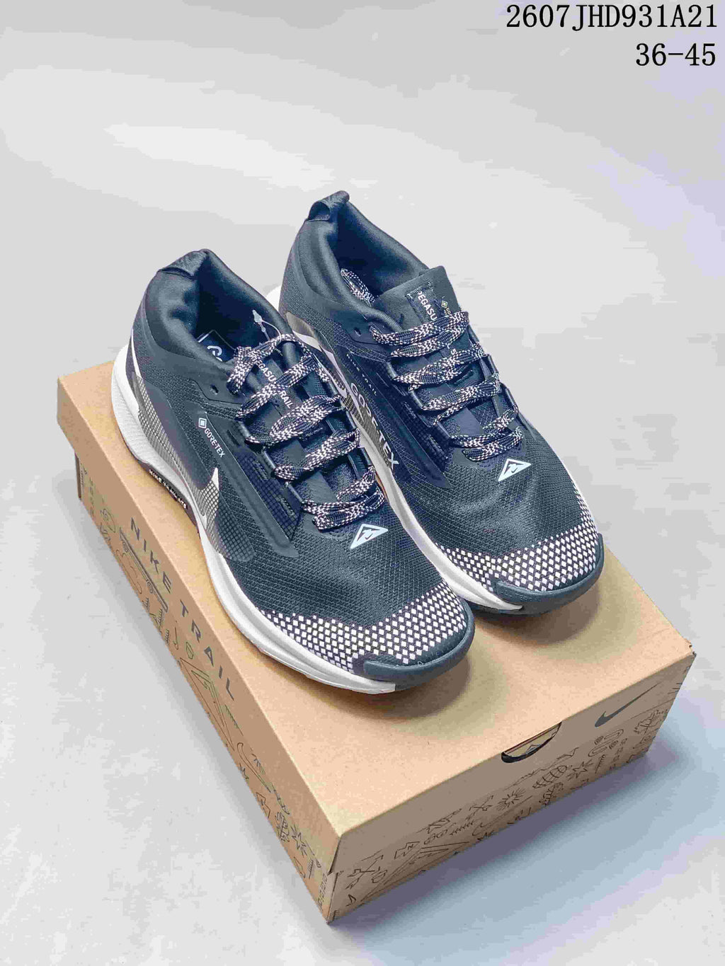 Pair of dark gray and black Nike trail sneakers displayed on a Nike shoebox, with white midsoles and checkerboard toe detailing.