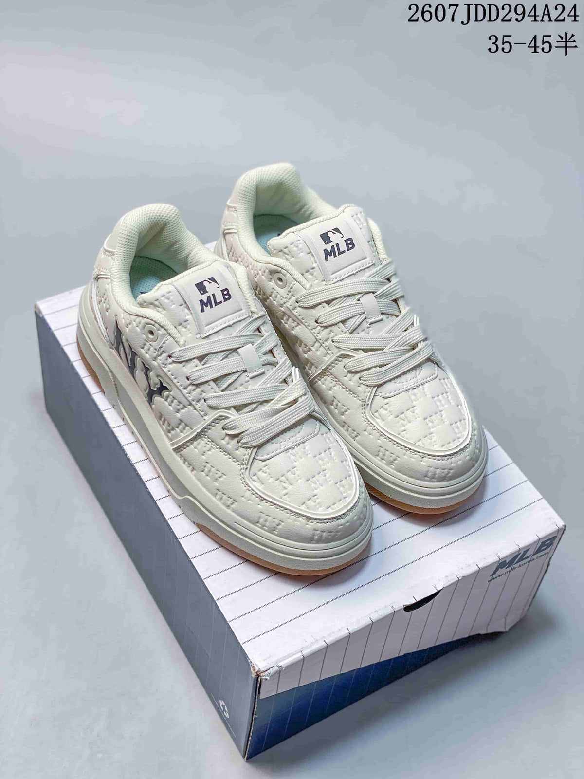 Pair of white MLB mid-top sneakers displayed on a shoebox, showing padded collars, lace-up fronts, raised soles, and gum-colored outsoles.