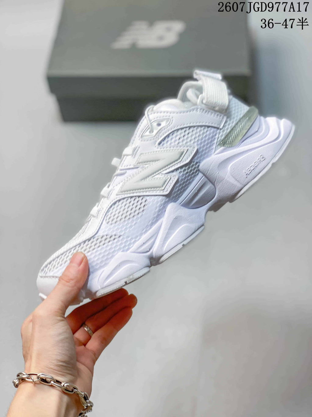 Side profile of the white New Balance 9060 sneaker showing mesh panels, layered branding, heel strap, and chunky sole.