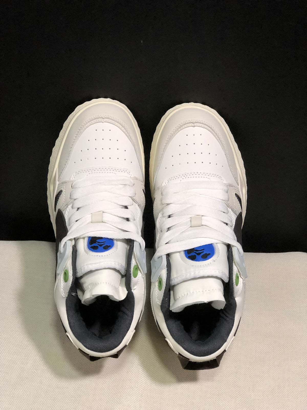 Top view showing the white laces, perforated toe boxes, blue tongue accents, and green eyelet details.