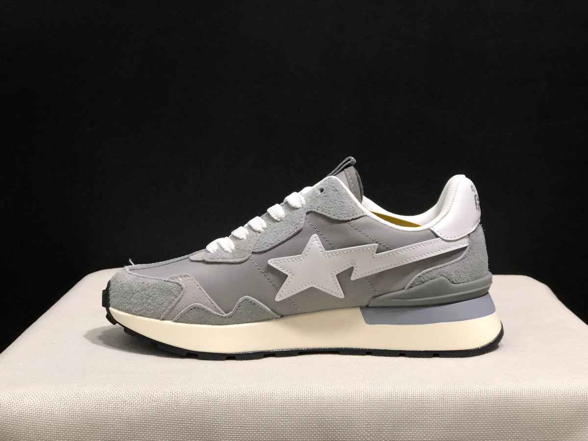 Side profile of a grey sneaker showing the large white star emblem, layered upper panels, cream midsole, and black outsole.