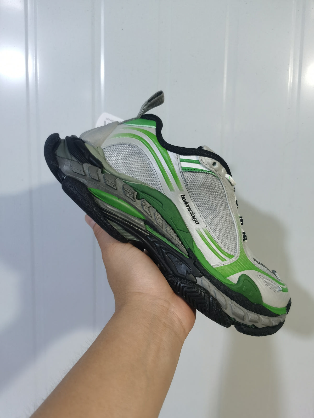 Close-up view of a grey and green Balenciaga Triple S 2 sneaker showing layered panels, mesh sections, black trim, and a chunky outsole.