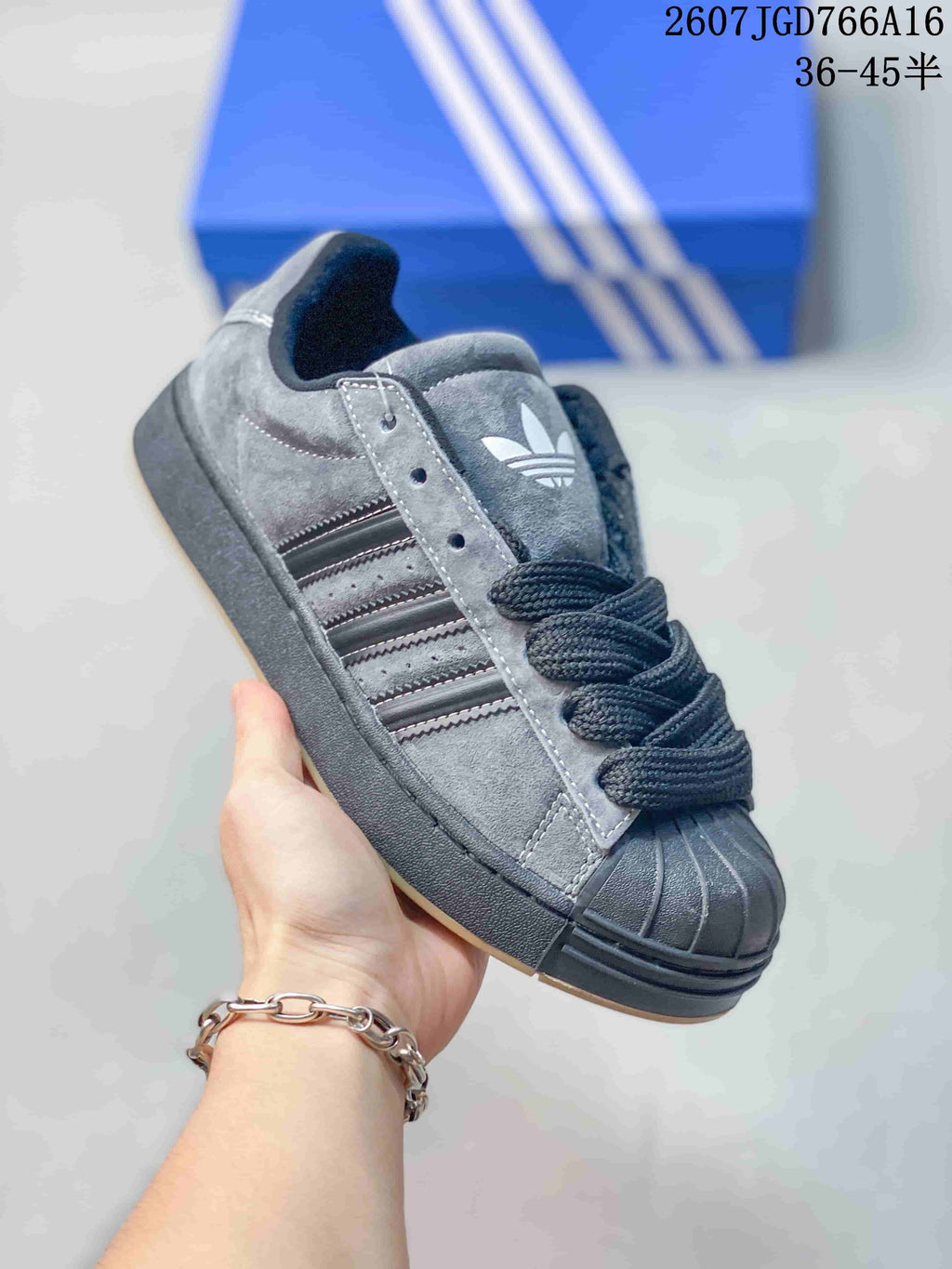 Close-up angled view of a gray and black adidas sneaker highlighting the trefoil tongue logo, three-stripe panel, laces, shell toe, and dark sole.