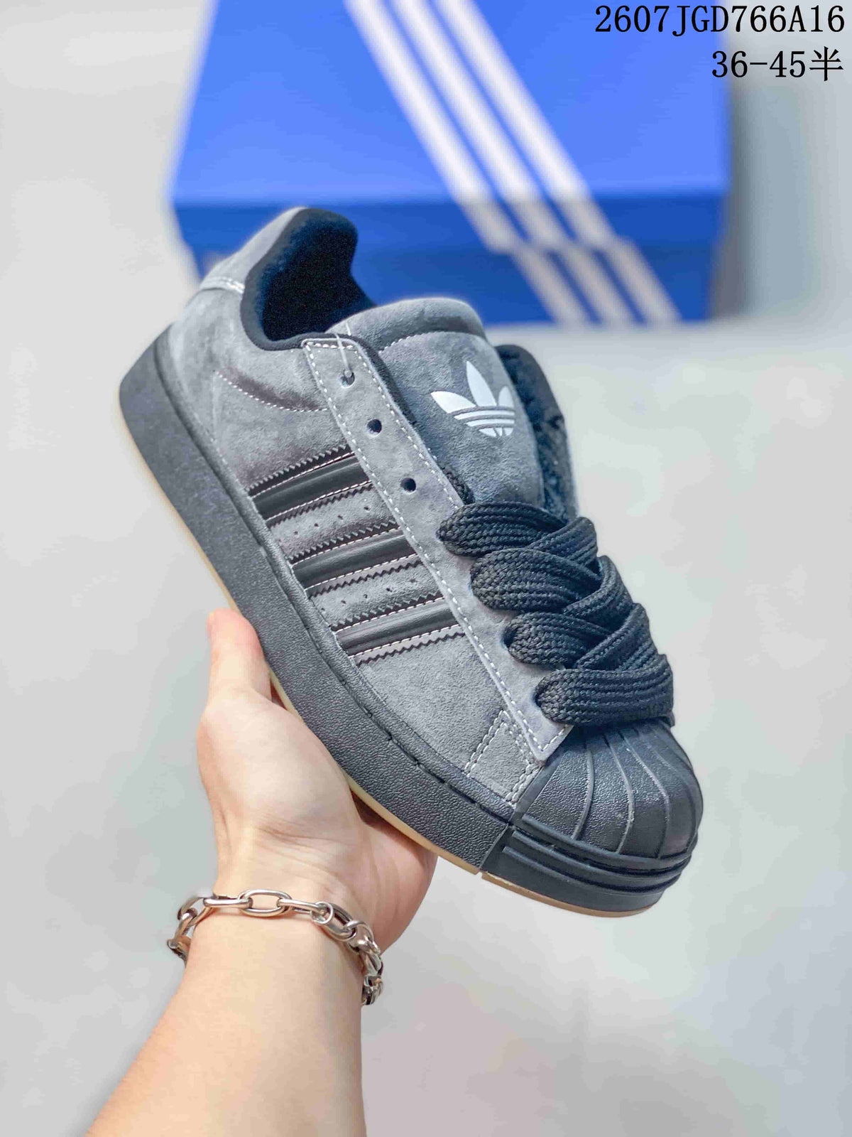 Close-up angled view of a gray and black adidas sneaker highlighting the trefoil tongue logo, three-stripe panel, laces, shell toe, and dark sole.