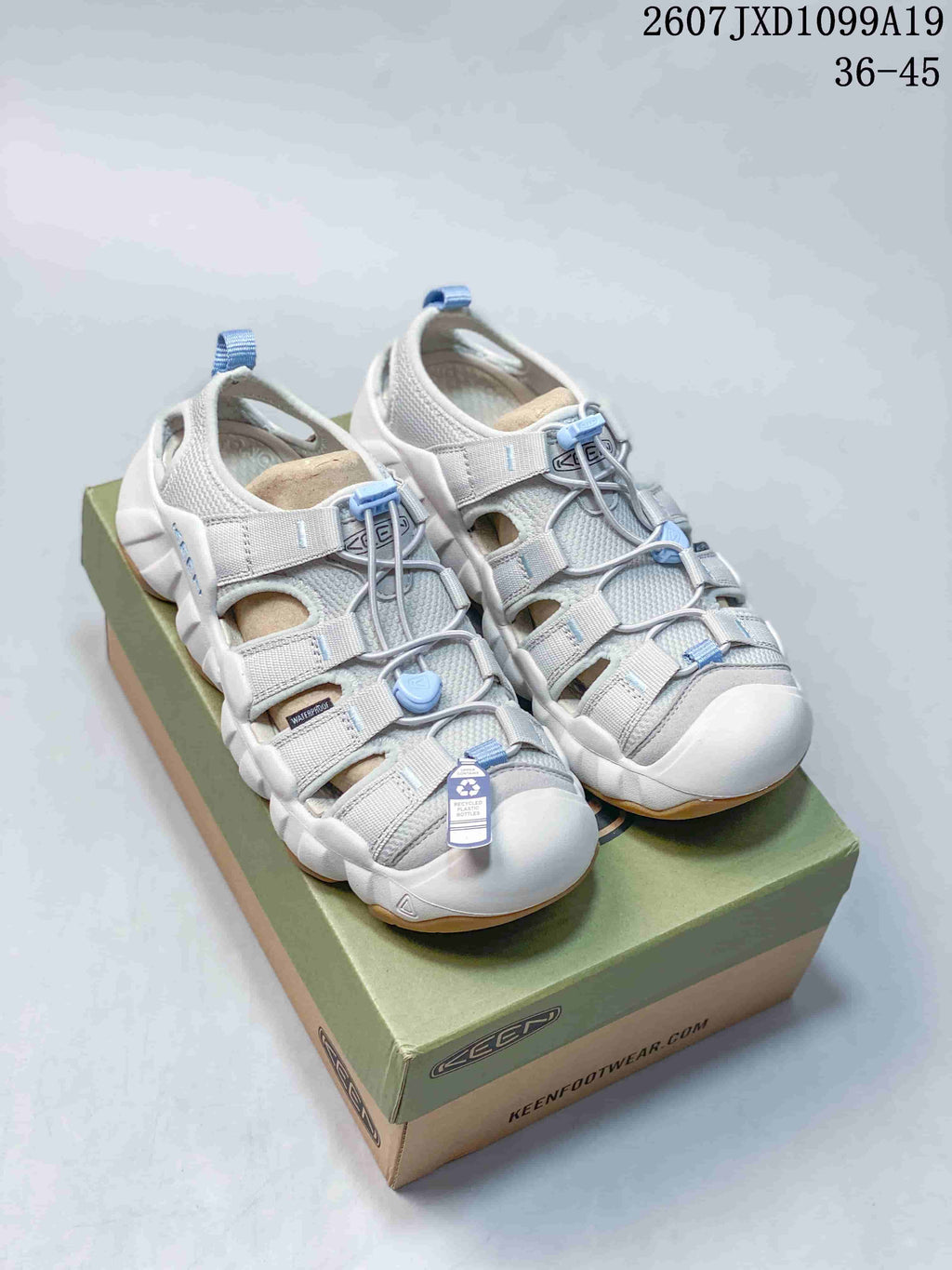 Pair of white and light gray KEEN Astoria West closed-toe sandals with blue accents displayed on a KEEN shoebox.