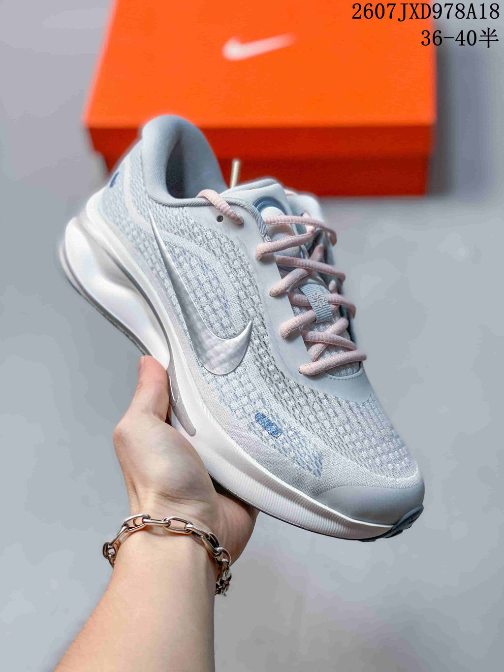 Angled side view of the light gray Nike Journey Run shoe showing the mesh upper, swoosh detail, pink laces and cushioned heel.