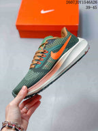 Side profile of a green Nike running shoe with an orange Swoosh, tan laces, white midsole, and textured outsole.