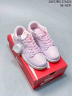 Pink and lilac Nike SB Dunk Low Pro sneakers displayed on a red shoebox, with a spare lace bundle visible.