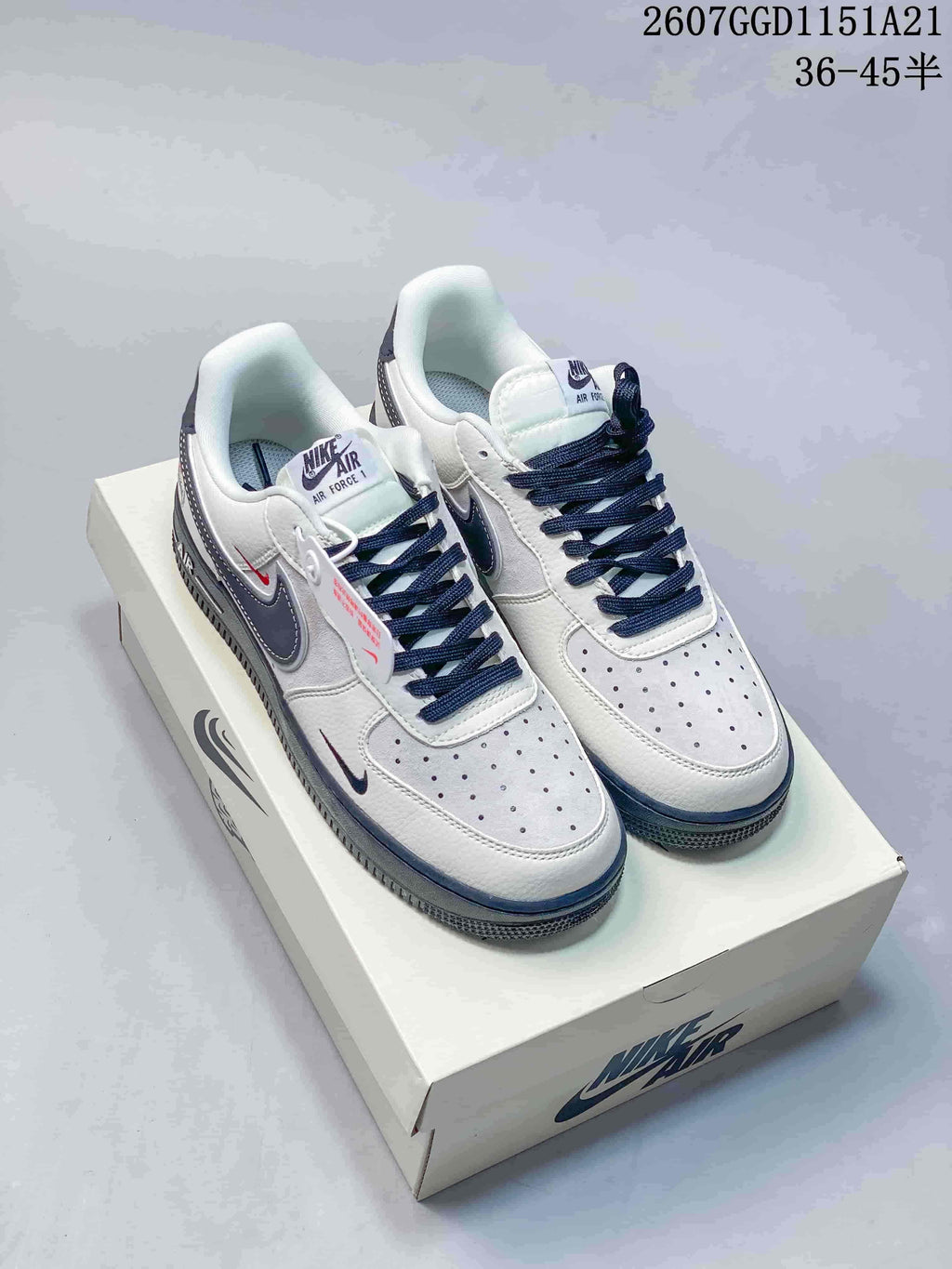 Pair of white and navy Nike Air Force 1 low-top sneakers displayed on a shoebox; image text shows style code 2607GGD1151A21 and size range 36–45.5.