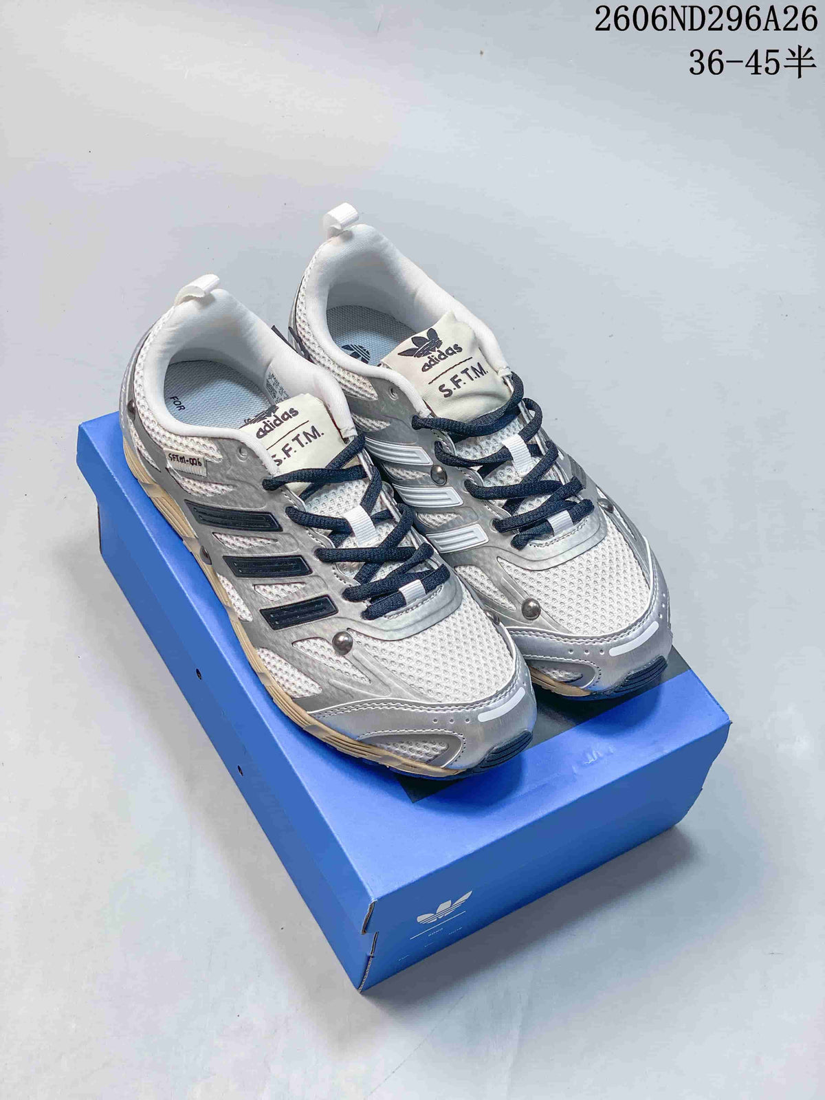 Pair of silver and white adidas Originals low-top sneakers with navy laces displayed on a blue shoebox.