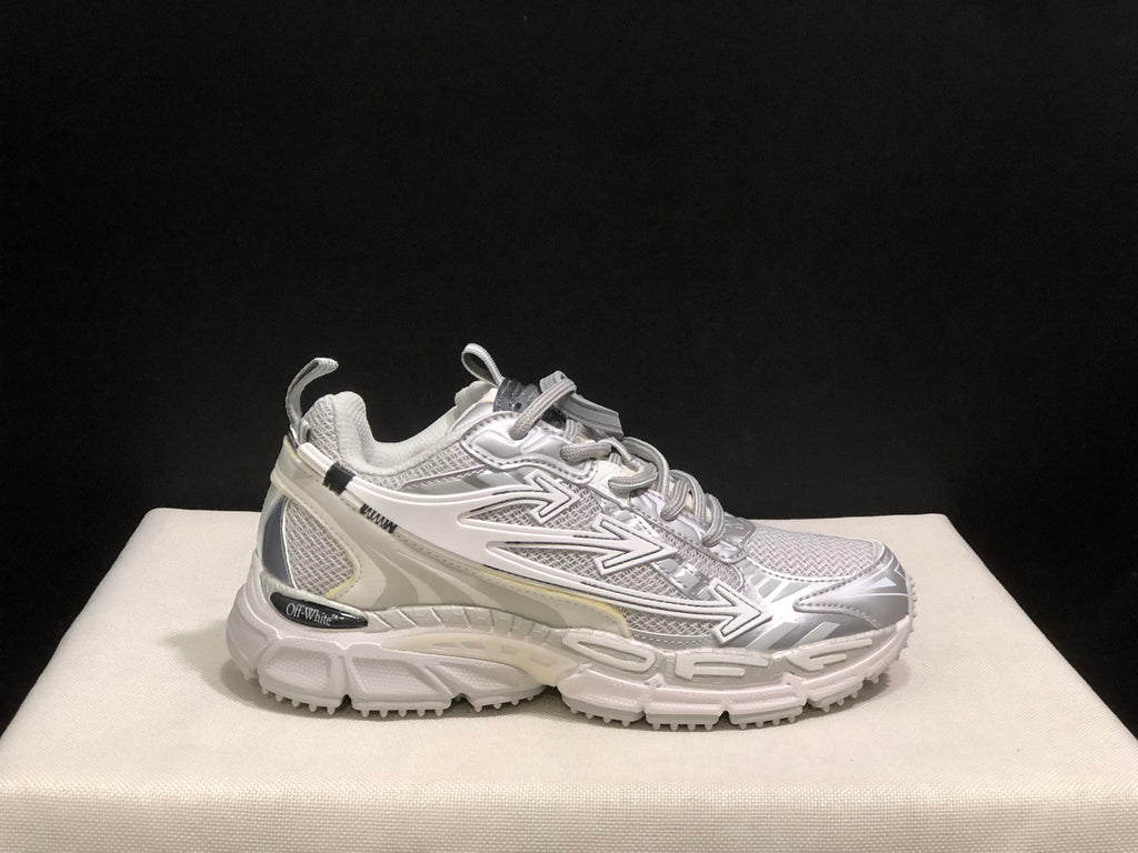 Close side profile highlighting the white and grey colorway, lace-up upper, directional graphics, and textured sole.