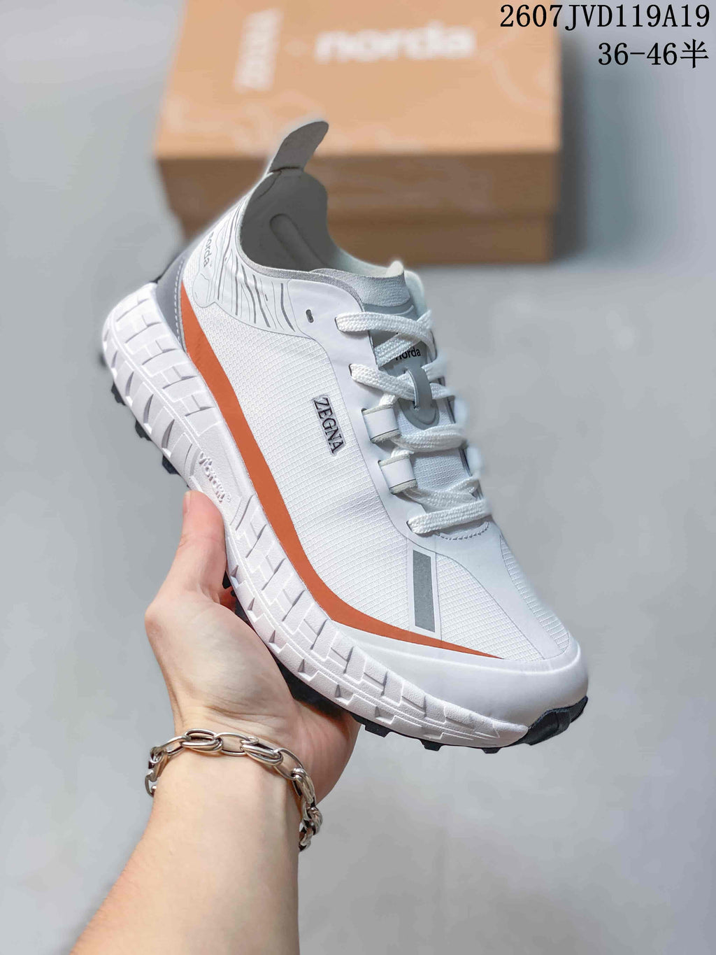 Angled side view of the white NORDA sneaker showing the orange side stripe, gray accents, lace-up closure, and black tread.