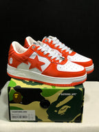 White and orange BAPE Sta sneakers displayed on a camouflage BAPE shoebox; the box label shows a photographed sample in EU 41 and CM 26.