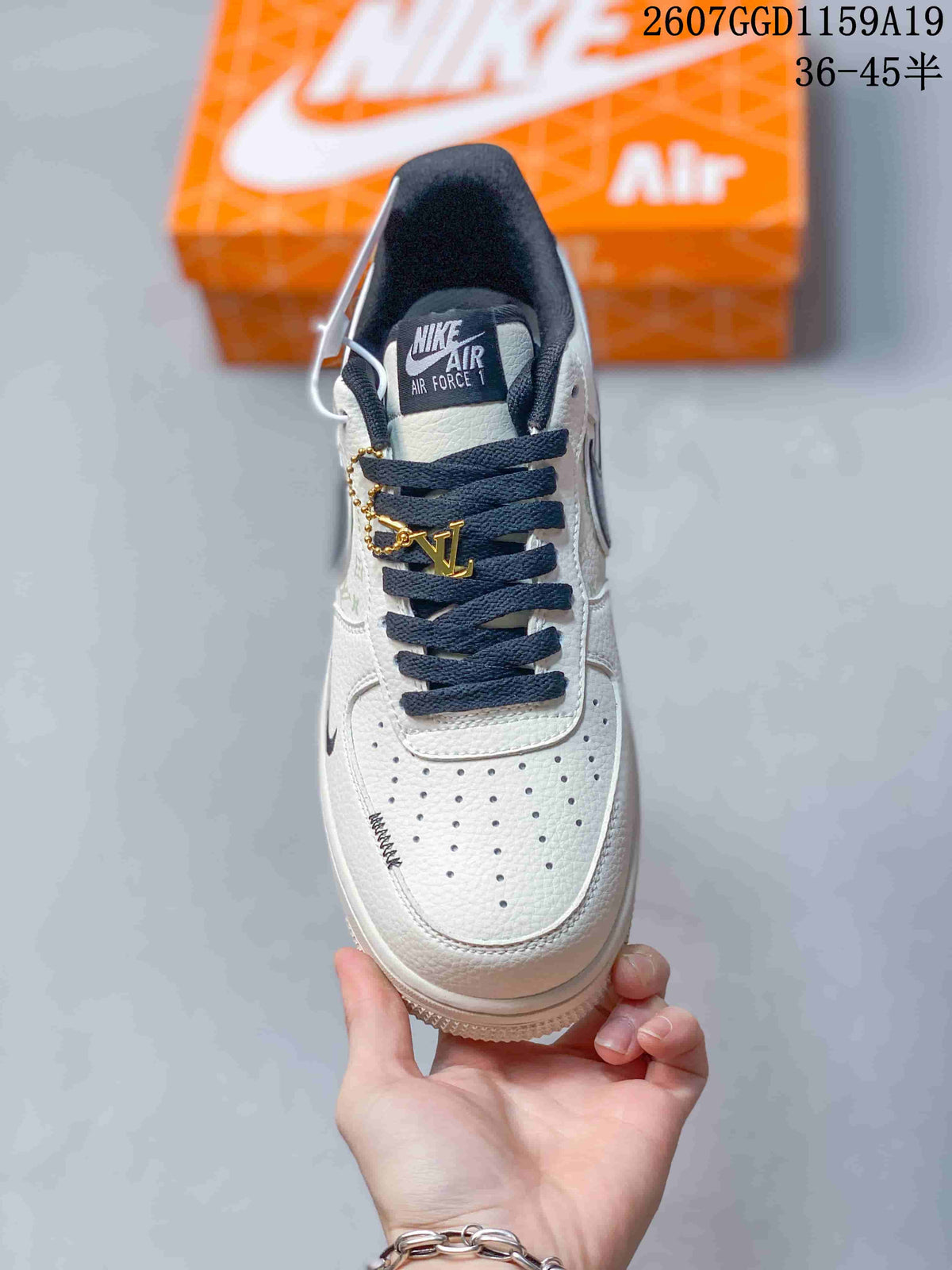 Top view of the white sneaker showing perforated toe panels, dark laces, black collar lining, and a gold-tone lace accessory.