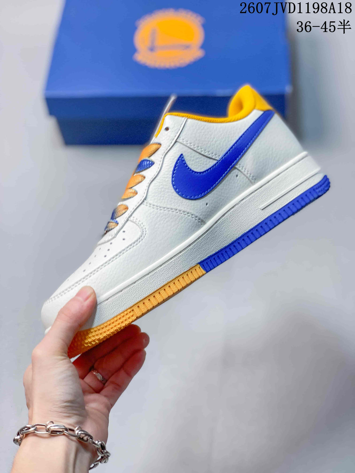 Side profile showing the white low-top upper, blue Swoosh, yellow outsole section, and blue outsole section.